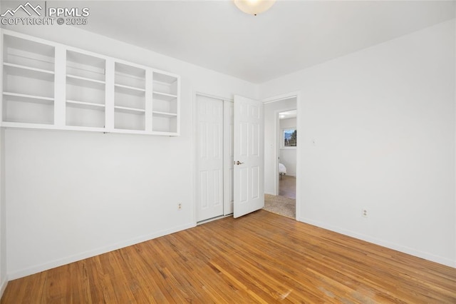 empty room with built in shelves and hardwood / wood-style flooring