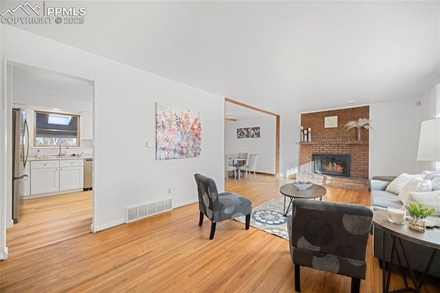 living room with a fireplace, sink, and light wood-type flooring