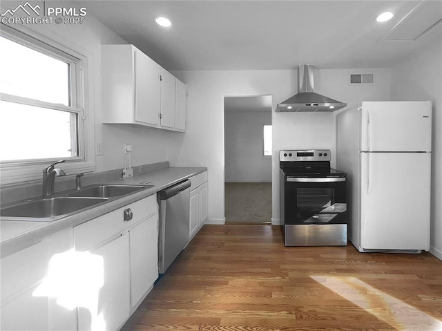 kitchen with white cabinetry, light hardwood / wood-style floors, appliances with stainless steel finishes, wall chimney range hood, and sink