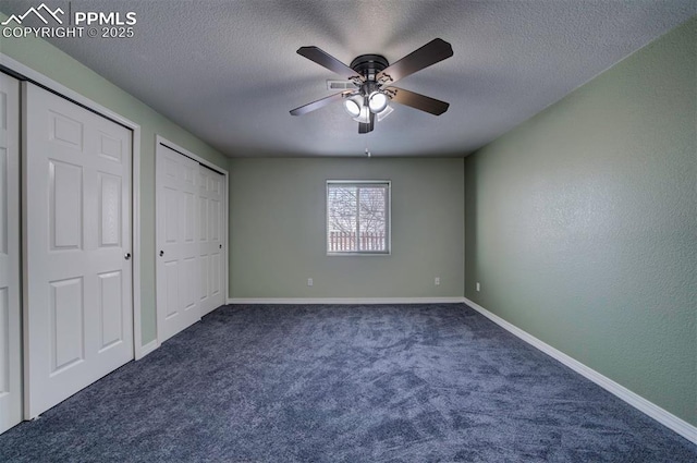 unfurnished bedroom featuring ceiling fan, dark carpet, a textured ceiling, and multiple closets