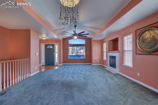 unfurnished living room featuring a tiled fireplace, ceiling fan with notable chandelier, vaulted ceiling, and dark colored carpet