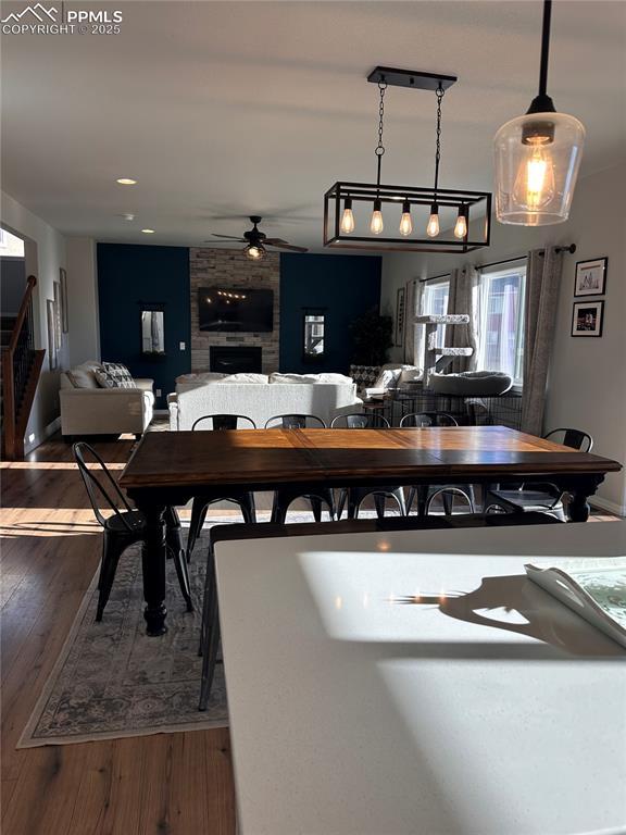 dining area featuring ceiling fan, hardwood / wood-style flooring, and a stone fireplace