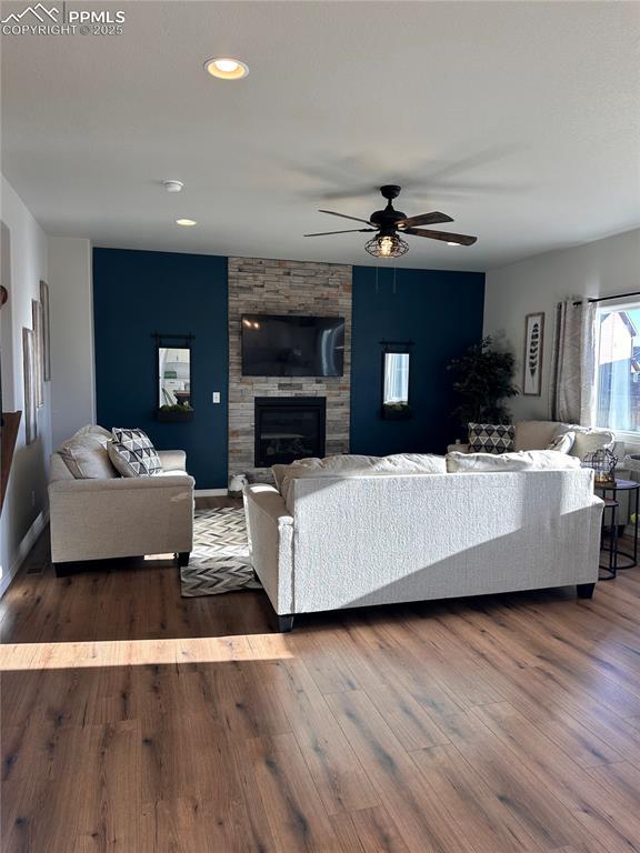 living room with ceiling fan, dark wood-type flooring, and a stone fireplace