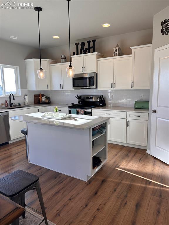 kitchen featuring hanging light fixtures, white cabinets, sink, and stainless steel appliances