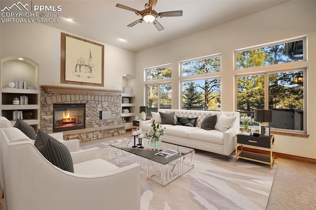 living room with ceiling fan, built in features, a towering ceiling, a fireplace, and carpet