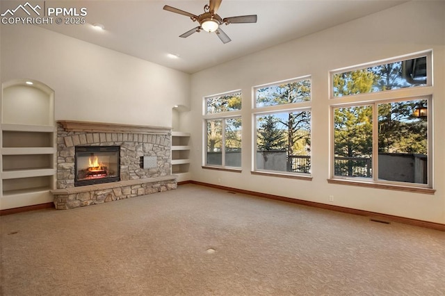 unfurnished living room featuring ceiling fan, a high ceiling, carpet flooring, built in shelves, and a stone fireplace