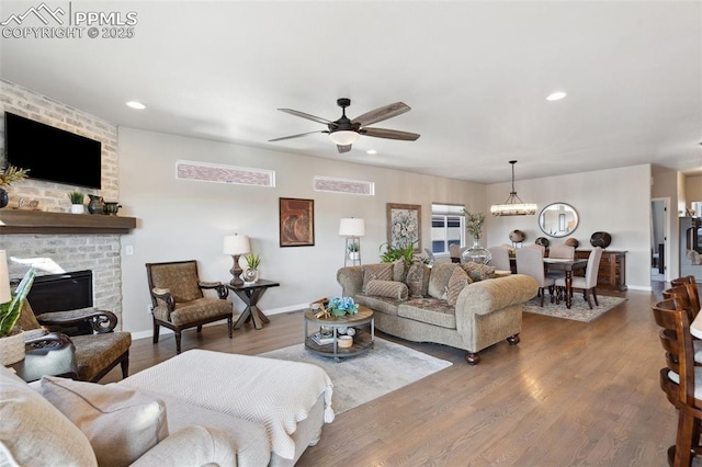 living room with ceiling fan with notable chandelier, hardwood / wood-style floors, and a brick fireplace