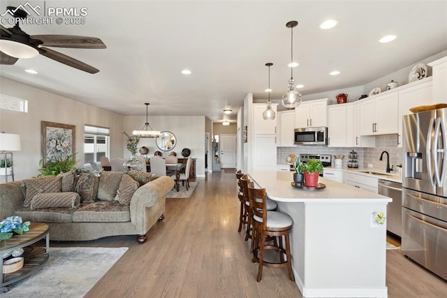 kitchen featuring stainless steel appliances, a center island, white cabinets, and decorative light fixtures