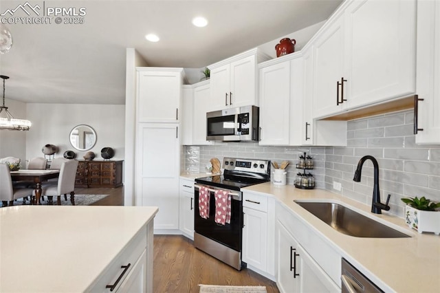 kitchen with white cabinetry, stainless steel appliances, decorative light fixtures, and sink