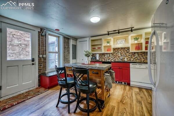 kitchen featuring dishwasher, a center island, decorative backsplash, light wood-type flooring, and stainless steel fridge