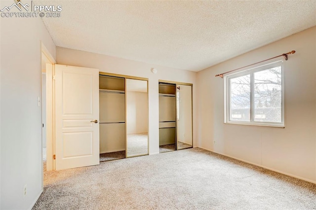 unfurnished bedroom featuring a textured ceiling, carpet, and two closets