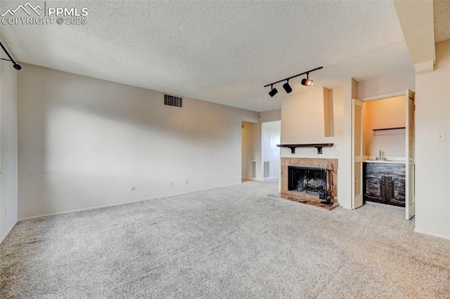 unfurnished living room with track lighting, carpet flooring, sink, and a textured ceiling