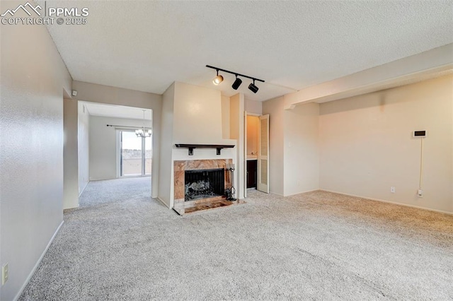 unfurnished living room featuring track lighting, light colored carpet, a fireplace, and a textured ceiling