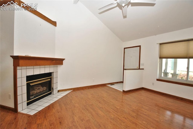 unfurnished living room with ceiling fan, high vaulted ceiling, a tiled fireplace, and light wood-type flooring