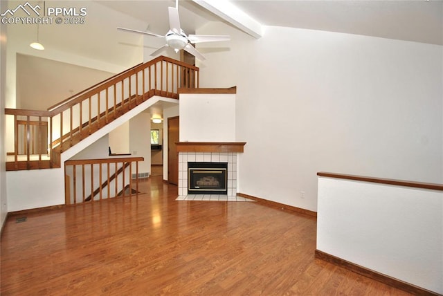 unfurnished living room featuring hardwood / wood-style flooring, ceiling fan, a tiled fireplace, and vaulted ceiling with beams