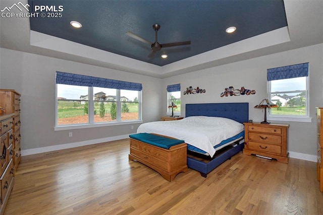 bedroom with ceiling fan, a tray ceiling, and light hardwood / wood-style floors