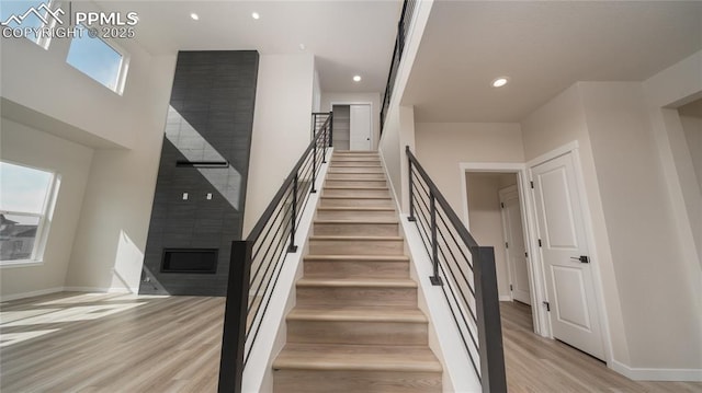 stairway with baseboards, a fireplace, wood finished floors, and recessed lighting