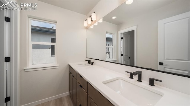 bathroom with double vanity, baseboards, a sink, and wood finished floors