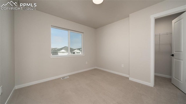 unfurnished bedroom featuring a walk in closet, visible vents, light carpet, and baseboards