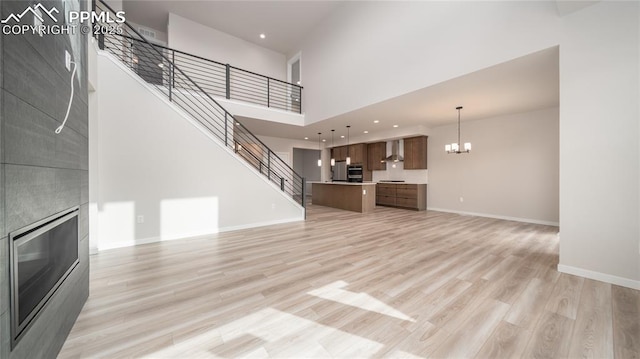 unfurnished living room featuring a large fireplace, a chandelier, light wood-type flooring, baseboards, and stairs