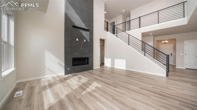 unfurnished living room with a large fireplace, visible vents, baseboards, stairs, and light wood-style floors