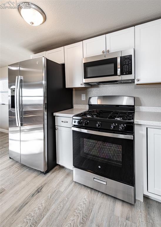 kitchen featuring white cabinetry, stainless steel appliances, light hardwood / wood-style floors, and a textured ceiling