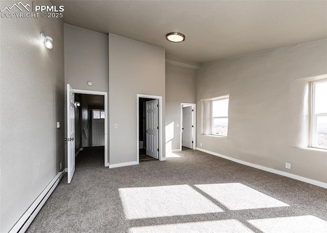 unfurnished bedroom featuring a baseboard radiator, carpet floors, and a towering ceiling