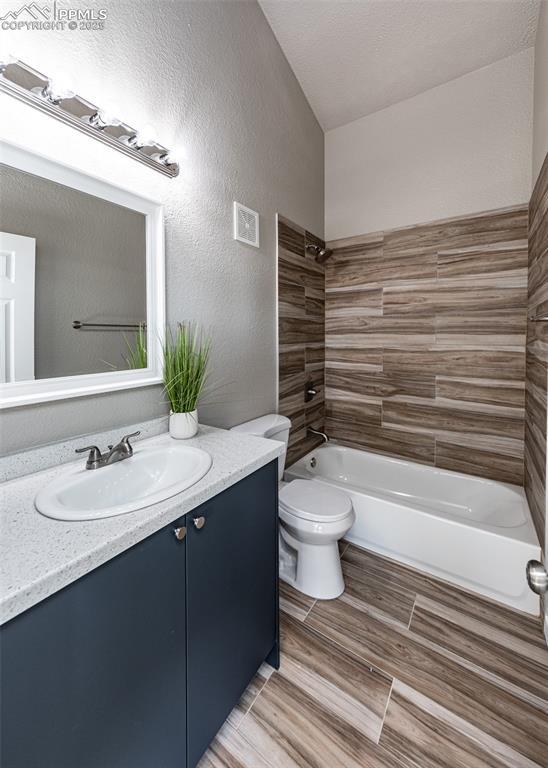 full bathroom featuring vanity, tiled shower / bath, and toilet