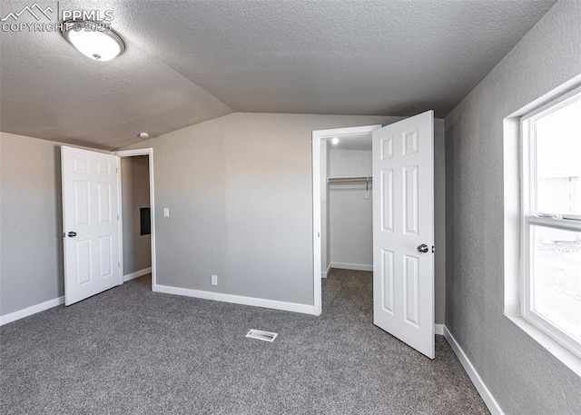 unfurnished bedroom with a spacious closet, vaulted ceiling, a textured ceiling, and dark colored carpet