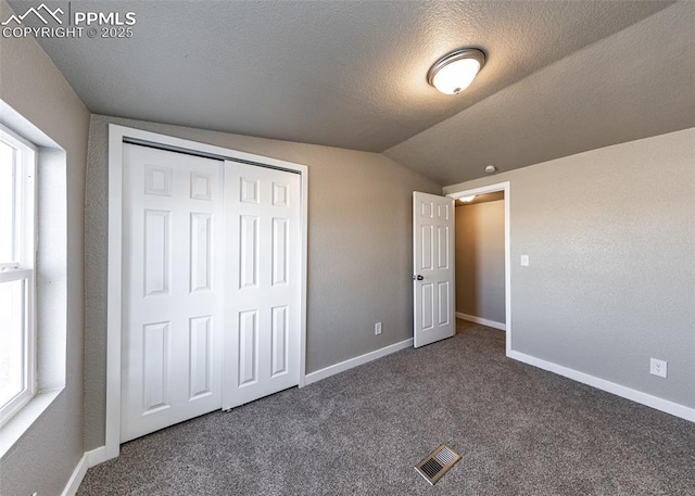 unfurnished bedroom with lofted ceiling, a closet, a textured ceiling, and dark colored carpet