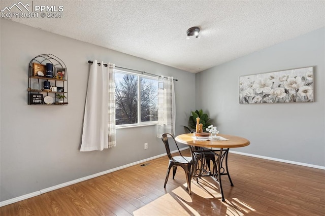 dining room featuring lofted ceiling, hardwood / wood-style flooring, and a textured ceiling