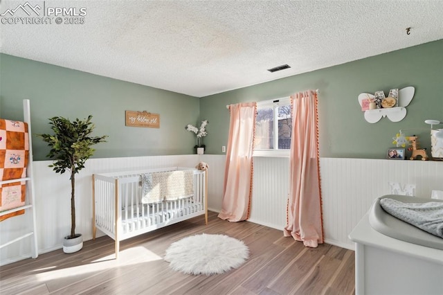 bedroom with wood-type flooring, a textured ceiling, and a crib