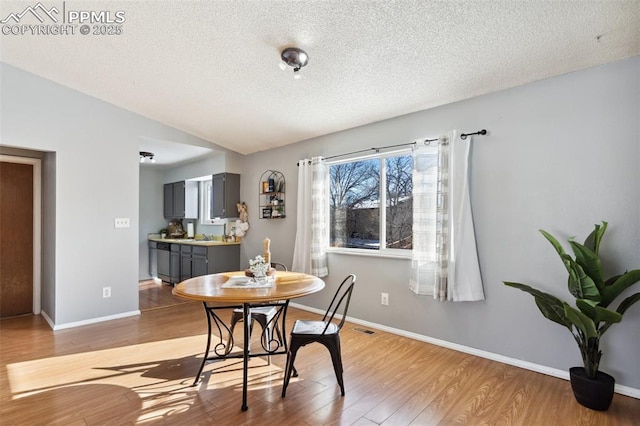 dining area with vaulted ceiling, a textured ceiling, and light wood-type flooring