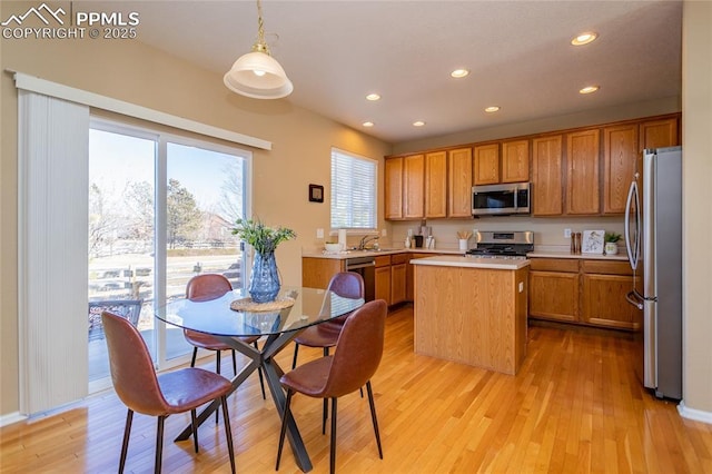 kitchen featuring light wood-type flooring, appliances with stainless steel finishes, hanging light fixtures, and a kitchen island