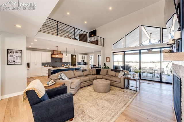 living room with light hardwood / wood-style flooring, a high ceiling, and a stone fireplace