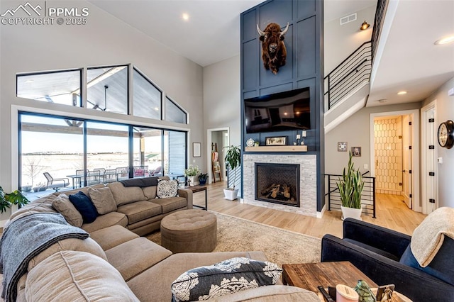 living room with light wood-type flooring, a fireplace, and a high ceiling