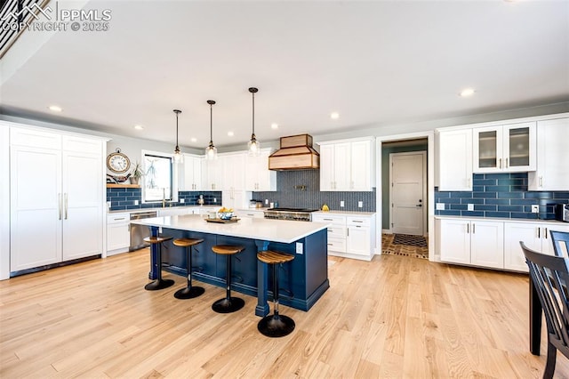 kitchen featuring a kitchen island, stainless steel dishwasher, white cabinetry, hanging light fixtures, and custom range hood