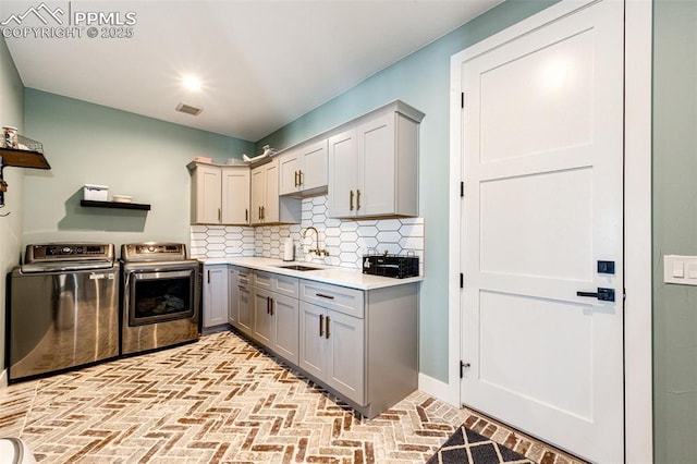 kitchen featuring decorative backsplash, sink, gray cabinets, and washing machine and clothes dryer