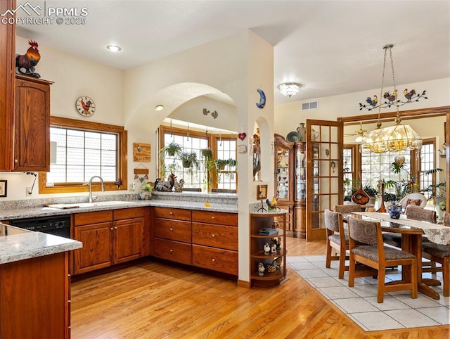 kitchen with sink, dishwasher, hanging light fixtures, light stone counters, and light hardwood / wood-style floors