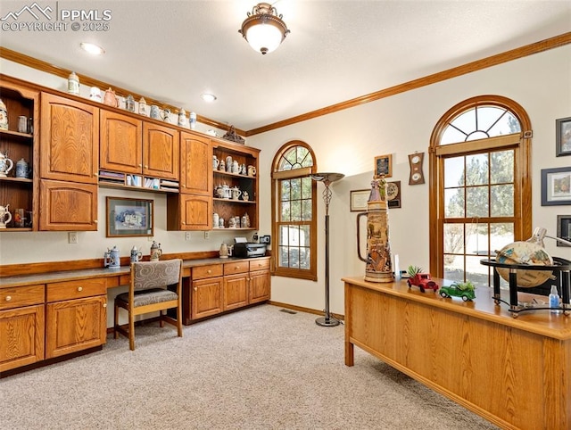 office space featuring a wealth of natural light, light carpet, ornamental molding, and built in desk