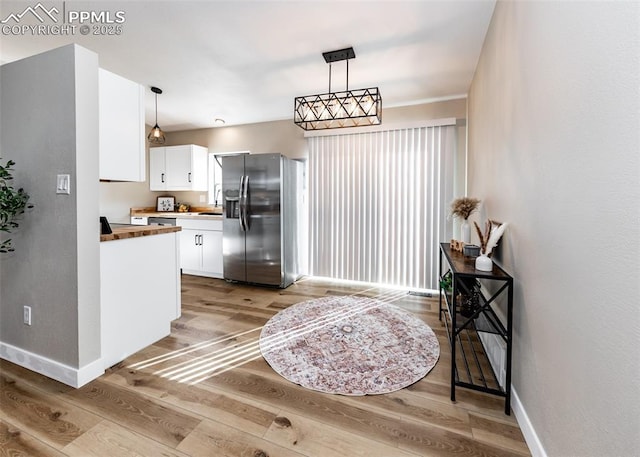 kitchen featuring decorative light fixtures, stainless steel refrigerator with ice dispenser, wood counters, and white cabinetry