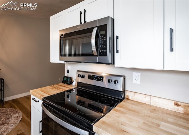 kitchen featuring hardwood / wood-style flooring, white cabinetry, appliances with stainless steel finishes, and butcher block countertops