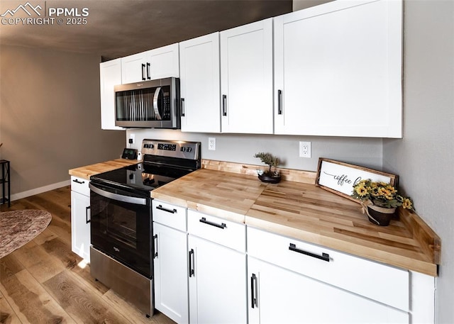 kitchen featuring light wood-type flooring, butcher block counters, appliances with stainless steel finishes, and white cabinetry