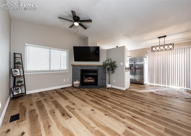 unfurnished living room featuring lofted ceiling, ceiling fan, a tile fireplace, and light hardwood / wood-style floors