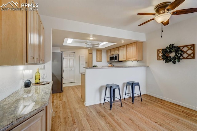 kitchen featuring a skylight, light wood-type flooring, light brown cabinets, a tray ceiling, and stainless steel appliances