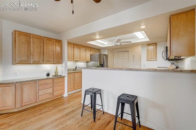 kitchen with light hardwood / wood-style flooring, a breakfast bar, ceiling fan, stainless steel fridge with ice dispenser, and a raised ceiling