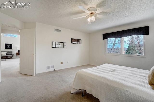 bedroom with ceiling fan, light colored carpet, and a textured ceiling