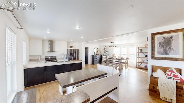 kitchen featuring white cabinets, wall chimney range hood, appliances with stainless steel finishes, and a healthy amount of sunlight