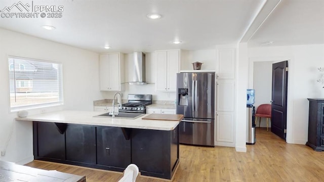 kitchen with appliances with stainless steel finishes, wall chimney range hood, white cabinets, kitchen peninsula, and light hardwood / wood-style flooring