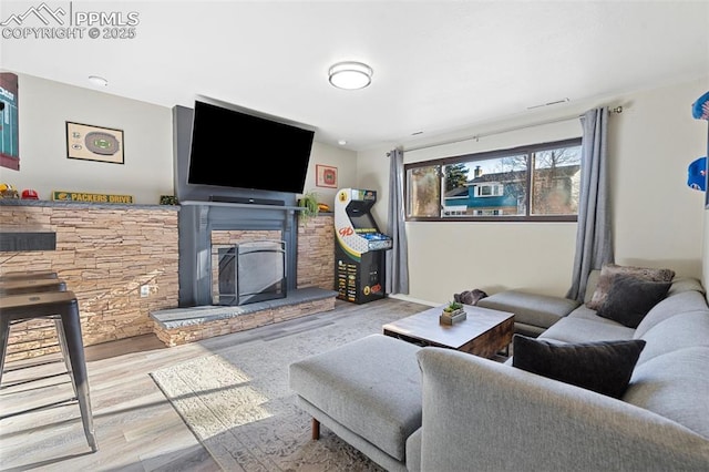 living room with a stone fireplace and light wood-type flooring